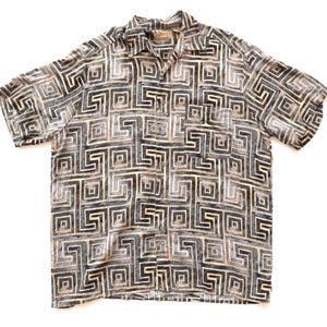 May include: Short-sleeved button-down shirt with a geometric pattern in shades of gray, black, and tan. The shirt has a collared neckline and a single chest pocket. The fabric appears to be lightweight.
