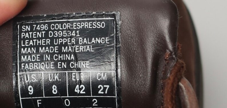 May include: A brown leather shoe with a size tag that reads "SN 7496 COLOR:ESPRESSO PATENT D395341 LEATHER UPPER BALANCE MAN MADE MATERIAL MADE IN CHINA FABRIQUE EN CHINE U.S. 9 U.K. 8 EUR 42 CM 27".