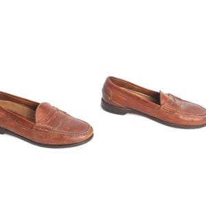May include: A pair of brown leather loafers with a penny strap detail. The loafers have a rounded toe and a low heel.