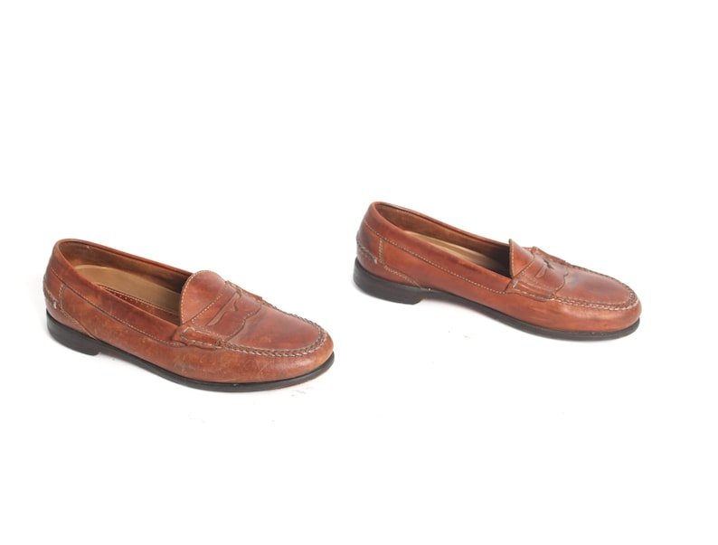May include: A pair of brown leather loafers with a penny strap detail. The loafers have a rounded toe and a low heel.