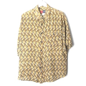 May include: A short-sleeved button-down shirt in a mustard yellow and dark gray color palette. The fabric features a repeating geometric pattern of interlocking oval shapes. The shirt includes a standard collar and a single chest pocket.