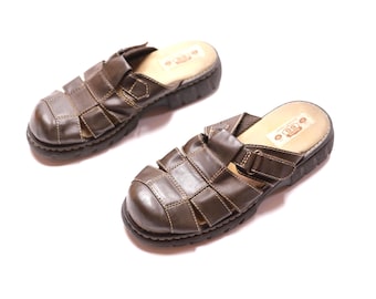 May include: A pair of brown leather sandals with a woven design. The sandals have a thick, dark sole and a light-colored insole. The sandals are approximately 10 inches long.