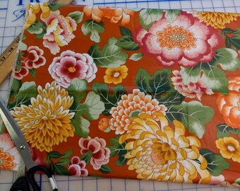 May include: A piece of fabric with a floral pattern. The fabric is orange with yellow, red, and white flowers. The flowers are surrounded by green leaves.