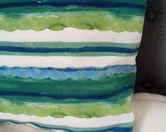May include: A white pillow with blue and green watercolor stripes. The pillow is on a white textured surface.