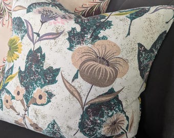 May include: Two decorative throw pillows with floral patterns. One pillow features a large beige flower with brown and green leaves on a cream background. The other pillow has a burgundy and beige floral design. Both pillows rest on a dark gray couch.