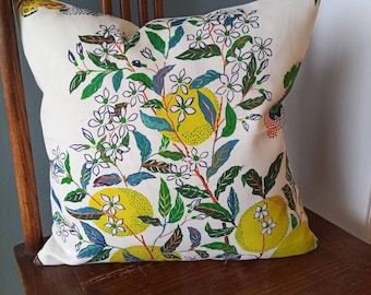 May include: A white pillow with a floral pattern featuring yellow lemons, green leaves, and white flowers. The pillow is on a wooden chair.