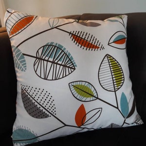 Könnte beinhalten: Ein weißes Kissen mit einem geometrischen Muster aus stilisierten Blättern in den Farben Türkis, Grün, Orange und Grau.