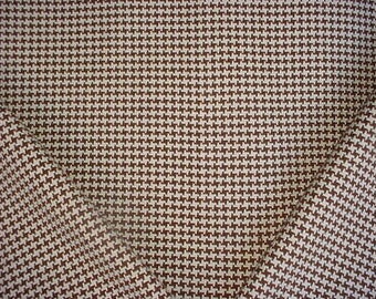 May include: A fabric featuring a repeating houndstooth pattern in dark brown and off-white. The textile displays a dense, woven texture with a consistent geometric design across the entire surface, showing a folded corner that reveals the pattern.