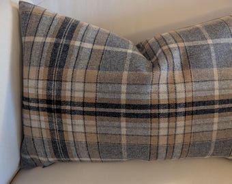 May include: A rectangular pillow with a plaid pattern in shades of gray, beige, and black. The pillow is placed on a white surface, suggesting a home decor item. The pillow's design is a classic plaid, suitable for various interior styles.
