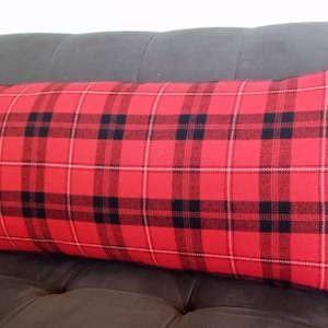 Op de afbeelding: Een rood en zwart geruit lumbaalkussen. Het kussen ligt op een grijze bank.