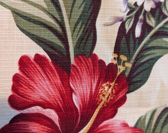 May include: Close-up of a floral fabric featuring a large red hibiscus flower with a yellow stamen. The design includes green leaves and smaller purple and white flowers on a cream-colored background.