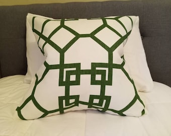 Può includere: Cuscino quadrato bianco con un motivo a traliccio geometrico verde. Il cuscino è posto su un letto bianco, con una testiera grigia sullo sfondo. Il cuscino misura circa 45 cm quadrati.