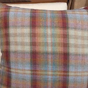 Op de afbeelding: Een plaid kussen met een bruin, rood, blauw en beige patroon. Het kussen is gemaakt van een zachte, textuurrijke stof.