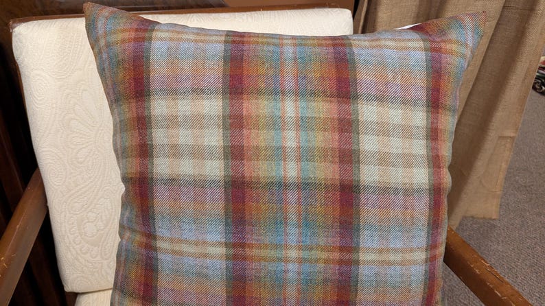 Op de afbeelding: Een plaid kussen met een bruin, rood, blauw en beige patroon. Het kussen is gemaakt van een zachte, textuurrijke stof.