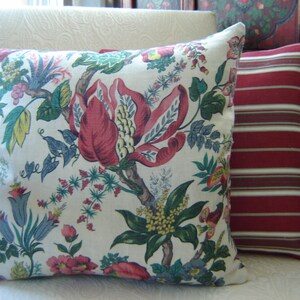 Pode incluir: Duas almofadas decorativas. Uma apresenta um fundo creme com um grande padrão floral em vermelho, rosa, verde e azul. A segunda almofada tem listras horizontais vermelhas e brancas.