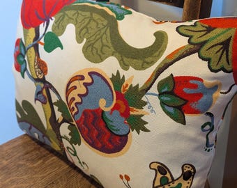 May include: A rectangular throw pillow featuring a cream-colored fabric base with a vibrant, multi-colored woven pattern. The design includes large red flowers, green foliage, blue swirling shapes, and a detailed butterfly with spotted wings.