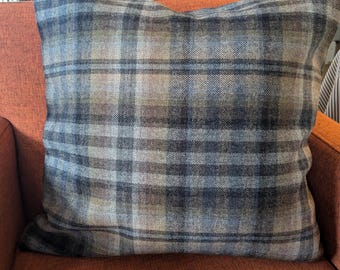 May include: A plaid throw pillow with a blue, brown, and beige color scheme. The pillow is sitting on a burnt orange couch.