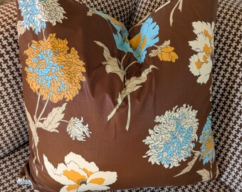 May include: A decorative throw pillow with a brown background and a floral pattern in shades of yellow, blue, and white. The pillow is placed on a houndstooth patterned surface.