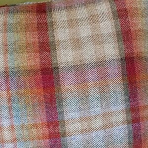 Op de afbeelding: Een close-up van een plaid kussen met een mix van rode, oranje, bruine en blauwe tinten. Het kussen is gemaakt van een zachte, textuurrijke stof.