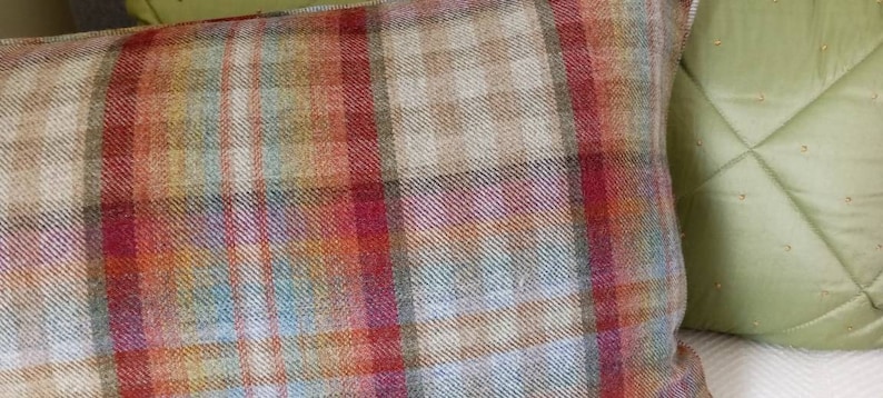 Op de afbeelding: Een close-up van een plaid kussen met een mix van rode, oranje, bruine en blauwe tinten. Het kussen is gemaakt van een zachte, textuurrijke stof.