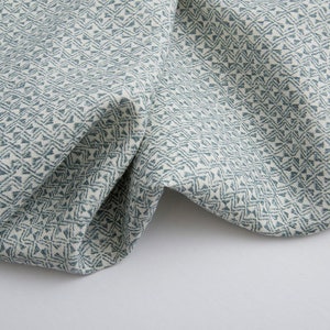 Op de afbeelding: Close-up van een witte stof met een blauw geometrisch patroon. De stof is gevouwen en heeft een textuur.