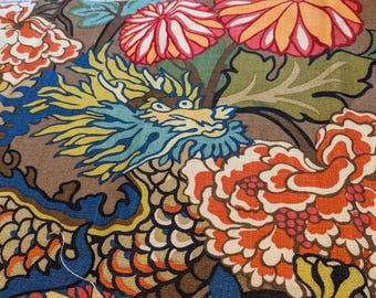 May include: Close-up of a fabric with a detailed dragon design. The dragon is blue and yellow, set against a brown background. Large orange and red flowers and green leaves surround the dragon, creating a vibrant pattern.