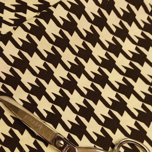 May include: A pair of silver scissors with the word "Chrome" and the number "8022" printed on the handle, lying on a white and black houndstooth fabric.