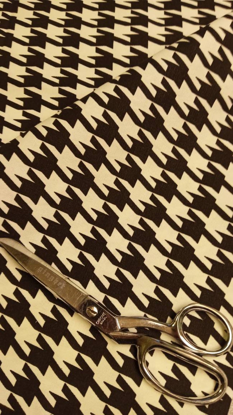 May include: A pair of silver scissors with the word "Chrome" and the number "8022" printed on the handle, lying on a white and black houndstooth fabric.