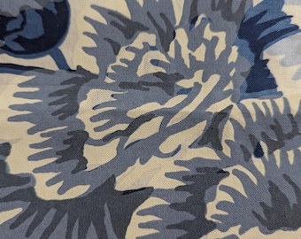 May include: A woven fabric featuring a large-scale floral pattern in shades of navy blue, slate blue, and light gray against a cream-colored background. The design consists of stylized, layered flower petals with visible textile weave texture.