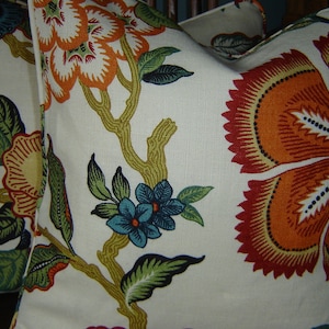 Op de afbeelding: Twee decoratieve kussens met een bloemenpatroon. De kussens hebben grote oranje en rode bloemen met groene bladeren en blauwe accenten op een crèmekleurige achtergrond. Het bloemmotief is gedrukt op een textuurstof.
