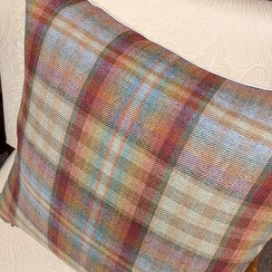 Op de afbeelding: Een plaid kussen met een bruin, rood en blauw kleurenschema. Het kussen is gemaakt van een zachte, textuurrijke stof en heeft een subtiele glans.