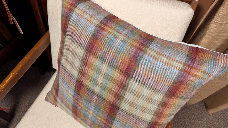 Op de afbeelding: Een plaid kussen met een bruin, rood en blauw kleurenschema. Het kussen is gemaakt van een zachte, textuurrijke stof en heeft een subtiele glans.