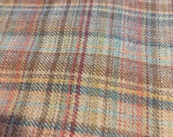 May include: Close-up of a woven fabric with a plaid pattern. The design features a mix of colors, including brown, blue, red, and yellow. The fabric has a textured appearance, suggesting a tweed or similar material.