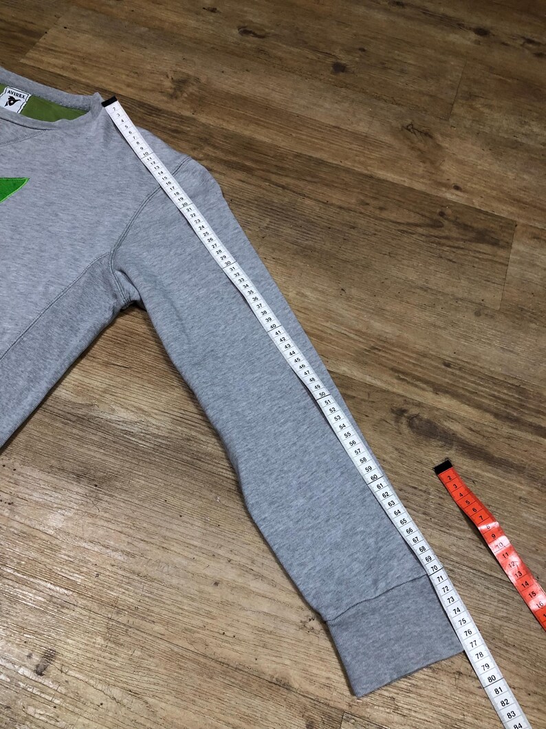 Puede incluir: Sudadera gris con un gr&aacute;fico verde en la parte delantera. La sudadera tiene un cuello redondo de canal&eacute; y mangas largas. La longitud de la manga se mide con una cinta m&eacute;trica.