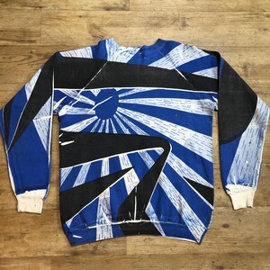May include: A blue and black long-sleeved sweatshirt with a graphic print of a sunburst design.