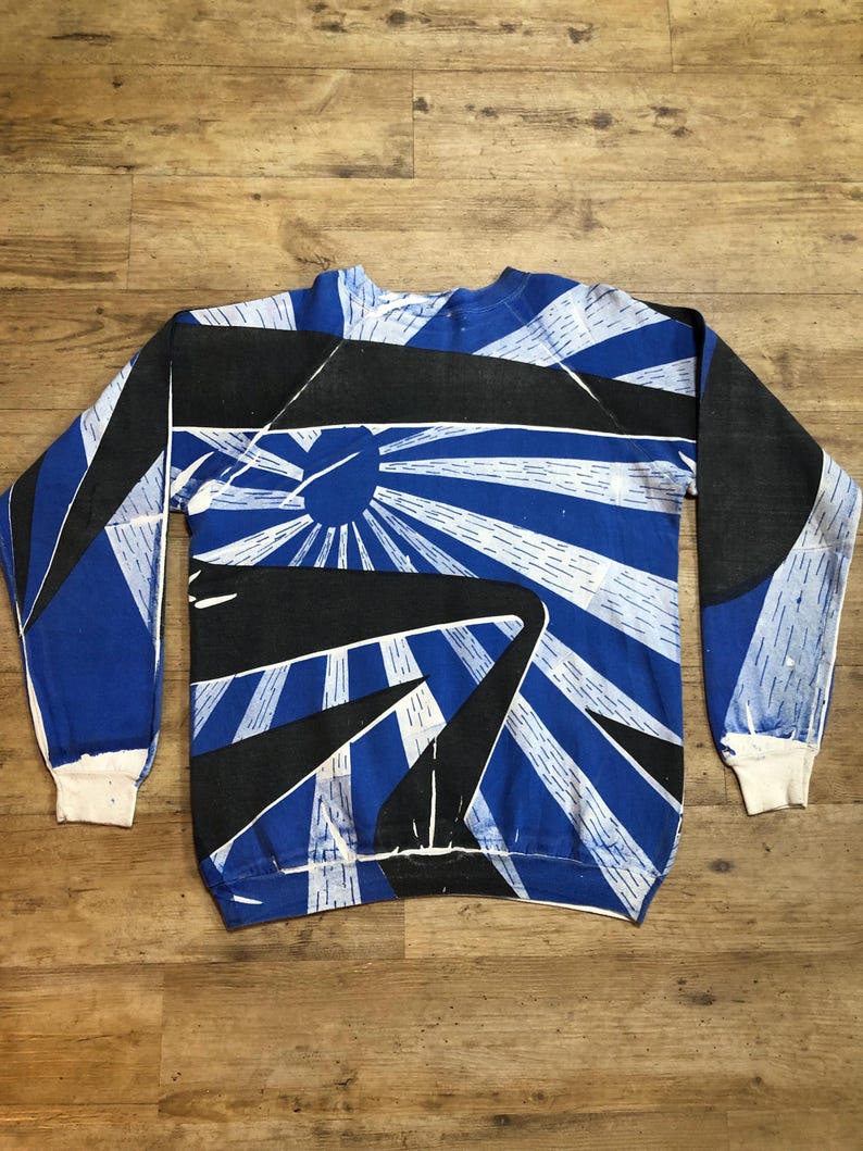 May include: A blue and black long-sleeved sweatshirt with a graphic print of a sunburst design.