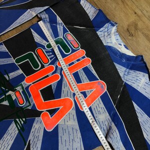 May include: A blue, black, and white long-sleeved shirt with a large orange and white graphic that says "7-11" on it. The shirt has a white tape measure running down the side, measuring 69 inches.