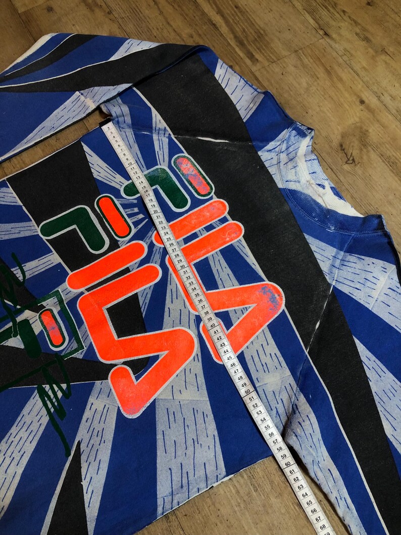 May include: A blue, black, and white long-sleeved shirt with a large orange and white graphic that says "7-11" on it. The shirt has a white tape measure running down the side, measuring 69 inches.