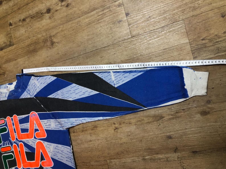 May include: A blue, black, and white long-sleeved shirt with a geometric pattern and the word "FILA" printed in red on the front.