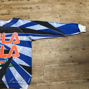 May include: A blue, black, and white long-sleeved sweatshirt with a graphic print of the word "FILA" in orange and white.