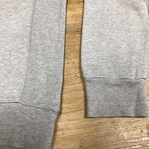 Puede incluir: Una sudadera gris con mangas largas y pu&ntilde;os de canal&eacute;. La sudadera est&aacute; hecha de una tela suave y c&oacute;moda.