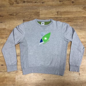 Puede incluir: Una sudadera gris con un gr&aacute;fico verde, azul y blanco de una tabla de surf con una estrella en ella. El texto "AWAKE" est&aacute; impreso debajo del gr&aacute;fico.