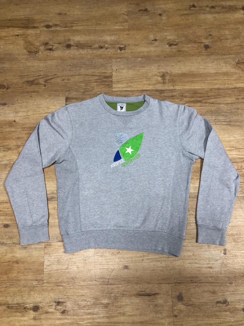 Puede incluir: Una sudadera gris con un gr&aacute;fico verde, azul y blanco de una tabla de surf con una estrella en ella. El texto "AWAKE" est&aacute; impreso debajo del gr&aacute;fico.