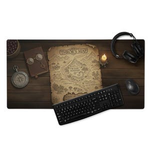 Puede incluir: Alfombrilla de escritorio con un mapa detallado etiquetado como "THROR'S MAP" con una cordillera y varias ubicaciones. La alfombrilla también incluye un teclado, un ratón, auriculares, una vela, una brújula y un libro con gafas.