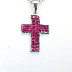 May include: A silver cross pendant with a red ruby stone inlay. The cross is set on a silver chain.