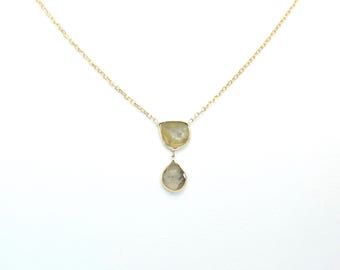 Puede incluir: Un delicado collar de oro con dos piedras preciosas. La piedra superior es de forma irregular y verde claro, y la piedra inferior tiene forma de lágrima. El collar está sobre un fondo blanco.