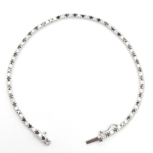 May include: A delicate tennis bracelet featuring alternating black and white gemstones set in a silver-toned metal. The bracelet is unclasped, showcasing the clasp mechanism. The gemstones are round-cut and evenly spaced.