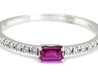 May include: A silver ring with a rectangular, deep pink gemstone at the center. The band is lined with small, clear gemstones. The ring is set against a white background, highlighting its elegant design and the sparkle of the gems.