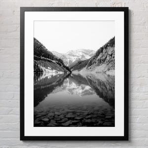 May include: A black and white photograph of a mountain lake with snow-capped peaks reflected in the water.