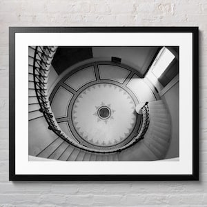 Può includere: Una fotografia in bianco e nero di una scala a chiocciola in un edificio con un soffitto a motivi. La scala è in pietra e ha una ringhiera in ferro battuto. Il soffitto è decorato con un motivo circolare.